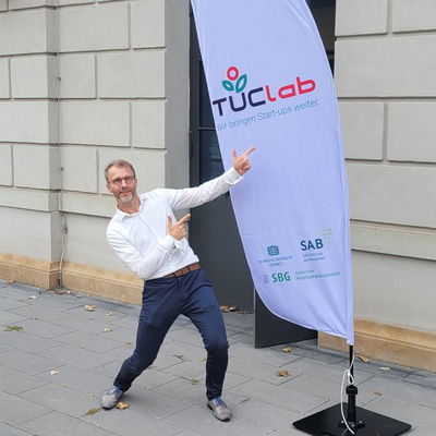 the photo shows co-founder of HETEROMERGE, Dr. Robert Kirchner, pointing to the TUClab logo on a flag.